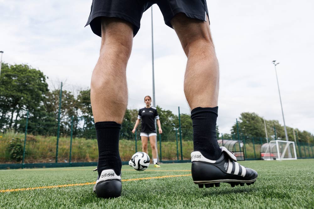 Low-angle photo between a footballers legs before they pass the ball a the player in the distance