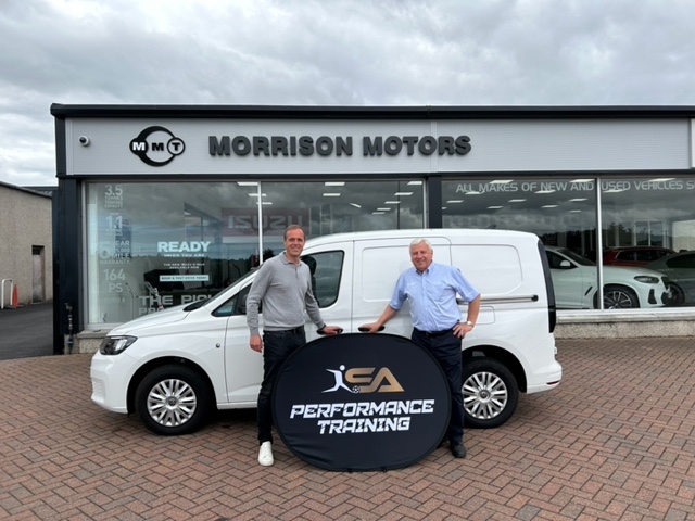 Scott Anderson posing with Brian Morrison outside of Morrison Motors in front of a white commercial van.